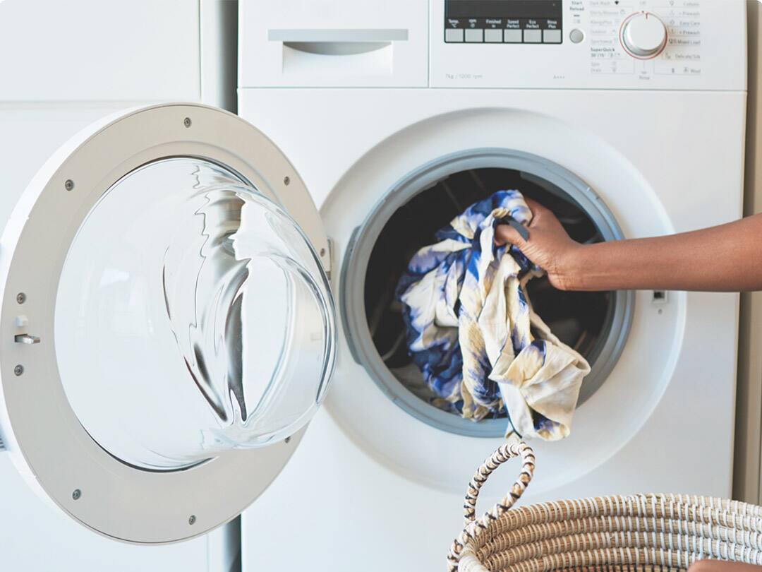 A woman placing a blouse in the washing machine.