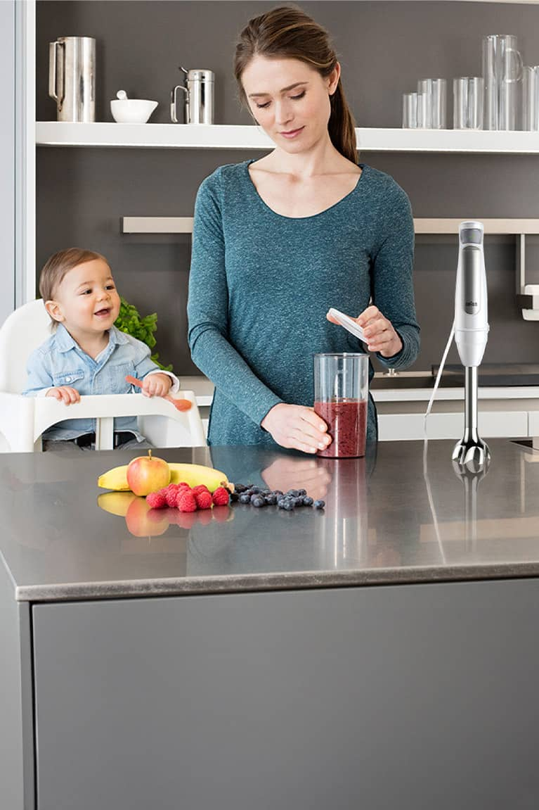 Young mother with toodler in the kitchen preparing red fruit purée