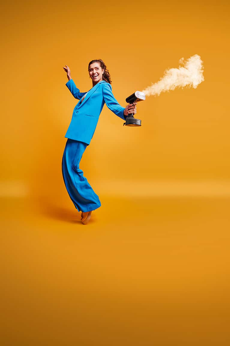 Young woman in blue suit holds a Braun QuickStyle 7 garment steamer