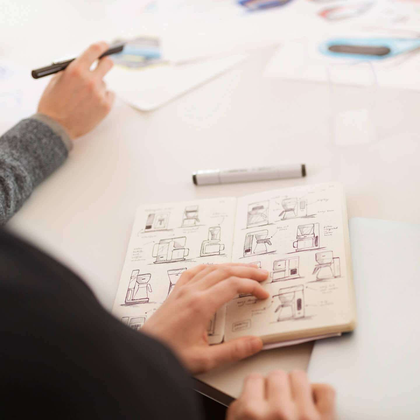 2 Designer at a table with coffeemachine sketches in a book.