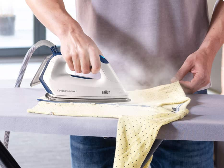 Close-up of a man ironing a yellow baby jacket