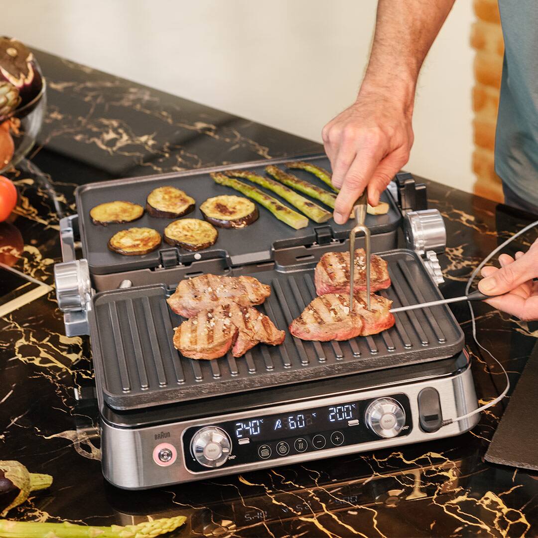 A man grilling steak alongside colorful vegetable