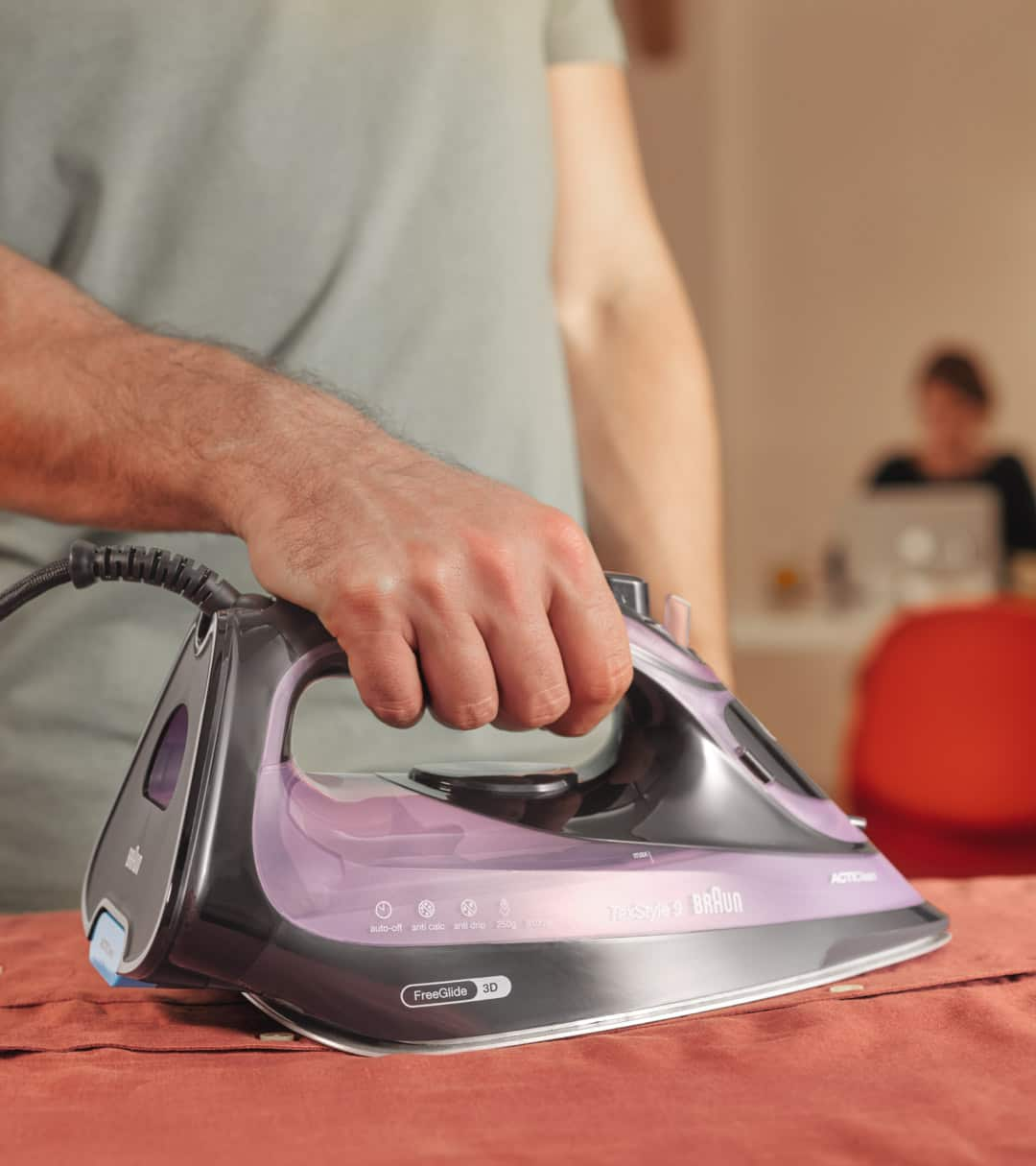 Man ironing red satin sheet with Braun TexStyle 9 Steam iron - close up